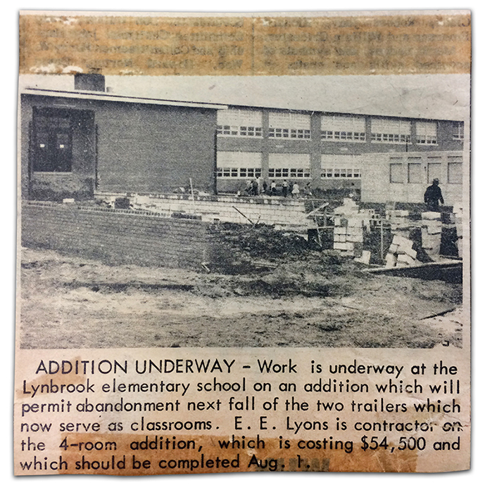Newspaper clipping, source and date unknown. There is a black and white photograph showing the progression of construction work on the new addition to Lynbrook. The foundation has been constructed and the brick and cinderblock walls are being erected. The walls are only about 3 feet high. In the distance, one of the trailers brought in to serve as a temporary classroom is visible, and some children can be seen playing near the school. The photograph has a caption which reads Addition Underway. Work is underway at the Lynbrook elementary school on an addition which will permit abandonment next fall of the two trailers which now serve as classrooms. E. E. Lyons is contractor on the 4-room addition, which is costing $54,500 and which should be completed August 1. 