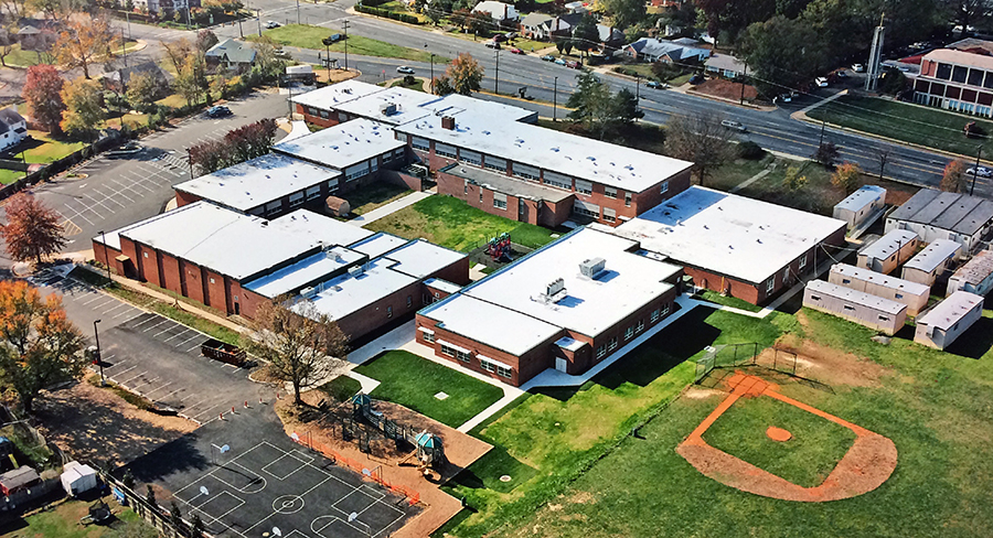 Aerial photograph of Lynbrook Elementary School taken from the northeast. The new addition is complete. The building is now square in shape with a large open courtyard in the center. Behind the school, a new blacktop with basketball courts has been constructed. Bright green grass is growing in the areas previously disturbed by construction equipment. The trailers are still visible on the far right of the photograph. The picture provides a very good vantage point to see the different sections of the building that have been added over the years. 