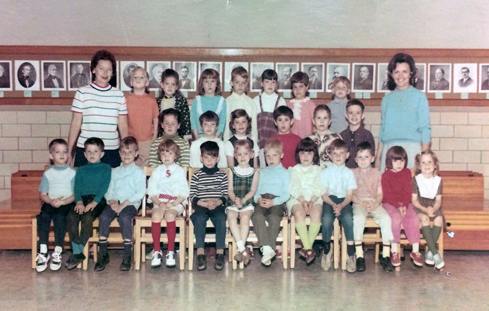 Color class photograph taken during the 1968 to 1969 school year. 25 children and two teachers are pictured. The children appear to be very young, perhaps kindergarten or first grade. They are arranged in three rows with one teacher on each side.