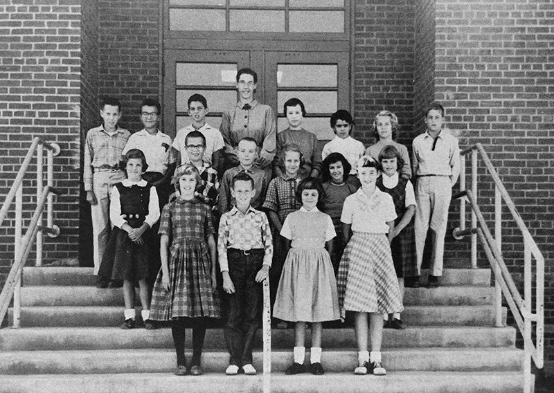 Black and white photograph from the 1959 to 1960 Memory Book showing Lynbrook's Student Cooperative Association. 17 children and their teacher sponsor are shown. They are standing on a stairway leading up to what at that time was the rear entrance to the school.  